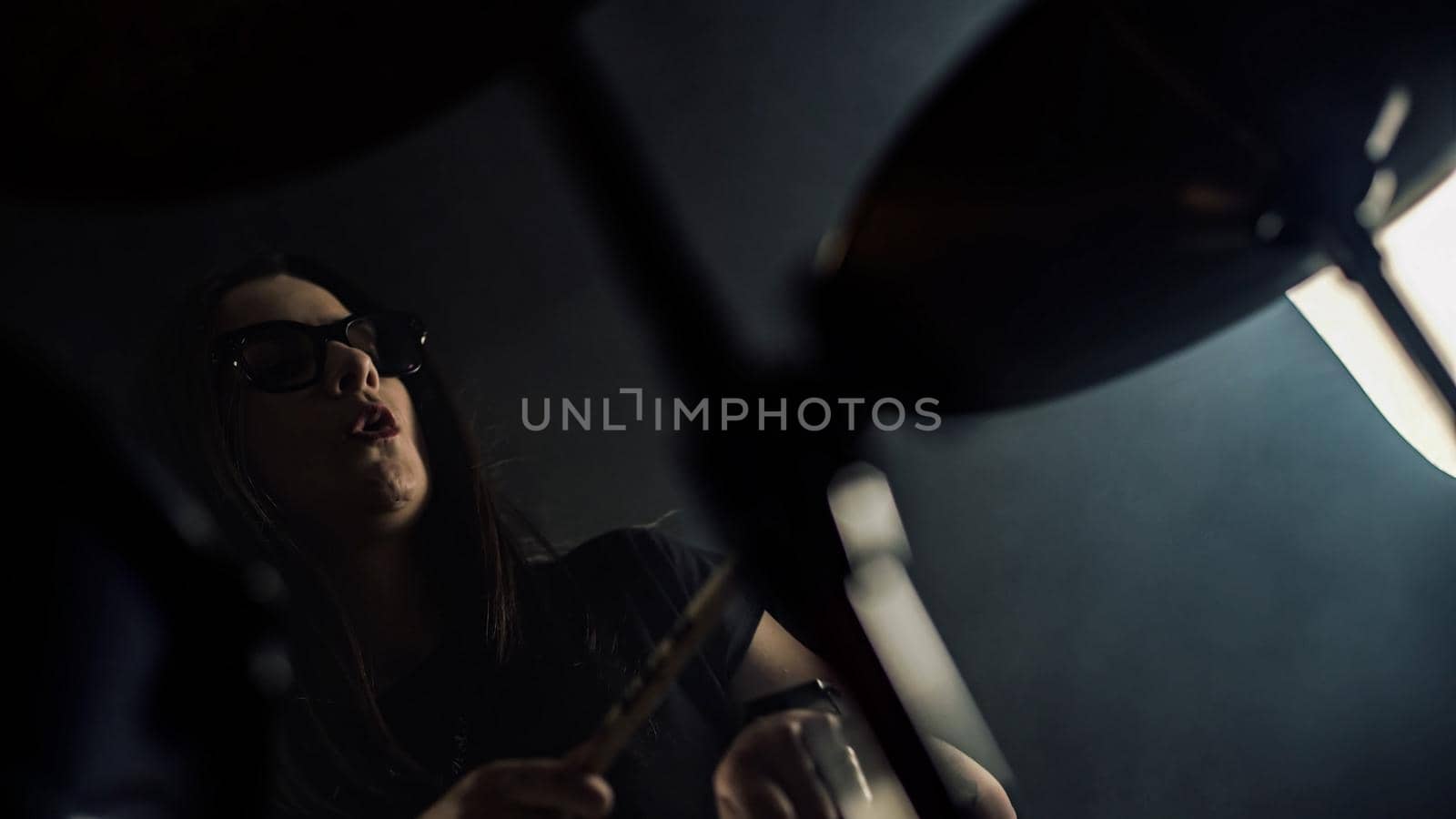 Young female drummer with spectacles plays a drum set holding drumstick in hands