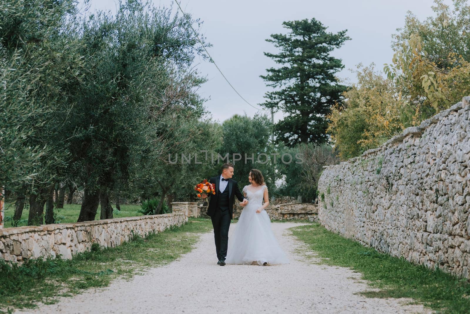 Happy stylish smiling couple walking in Tuscany, Italy on their wedding day. The bride and groom walk down the street by the hands. A stylish young couple walks. Husband and wife communicate nicely. Lovers run through the streets of the city.