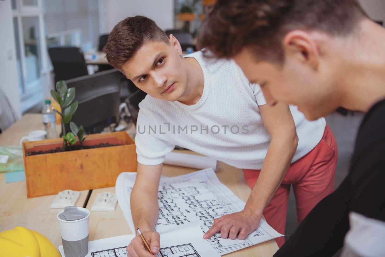 Architects office, building construction concept. Handsome male engineer working on a building sketch with his colleague