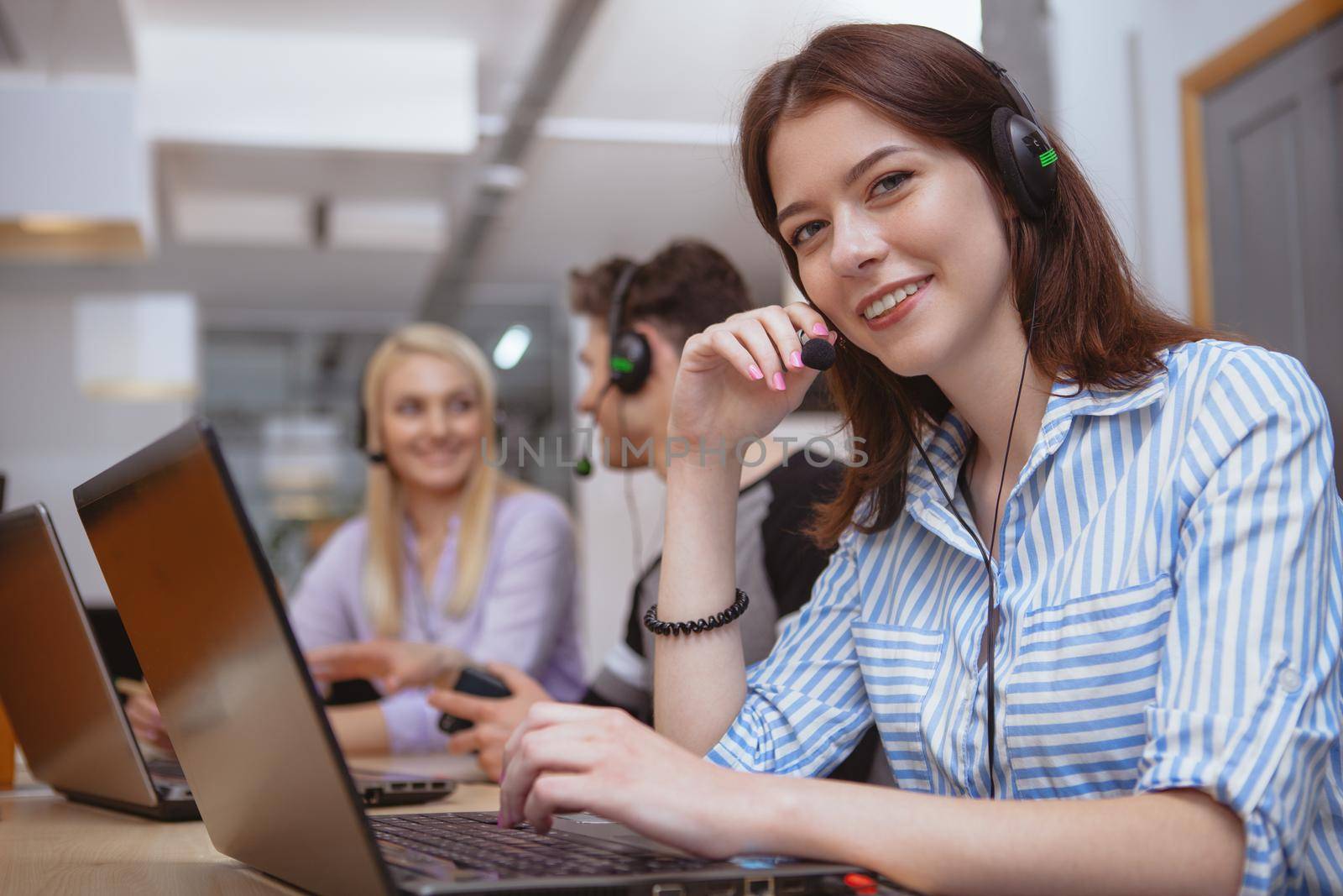 Attractive cheerful female call center worker wearing headset with microphone smiling to the camera. Lovely woman enjoying working at customer support service, smiling to the camera, copy space