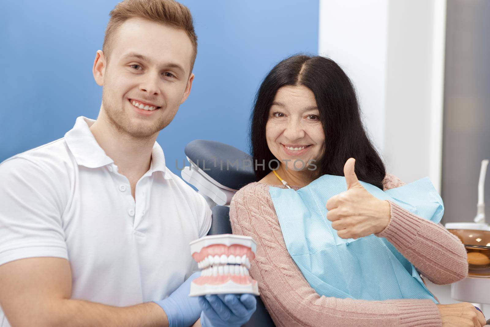 Perfectly healthy! Senior woman smiling happily showing thumbs up at the dental clinic her dentist smiling to the camera holding teeth mold profession communication trust medicine people dentistry