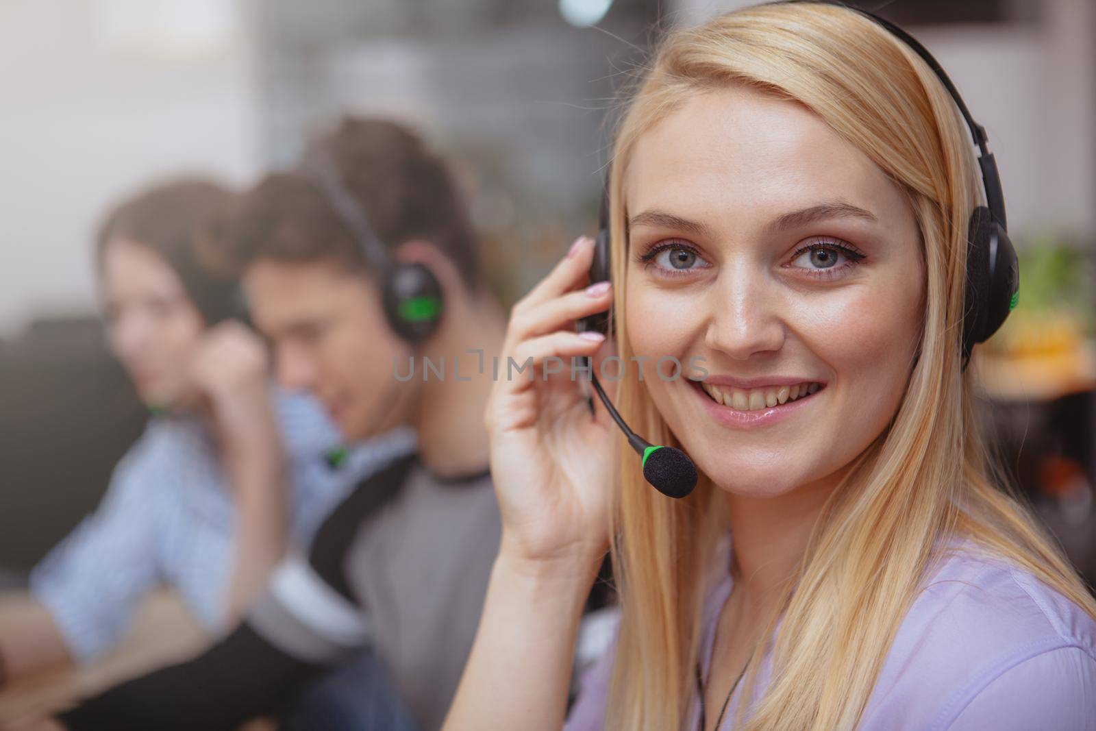 Close up of a happy beautiful young woman enjoying working at customer support call center. Attractive female customer services operator wearing headset with microphone, smiling to the camera