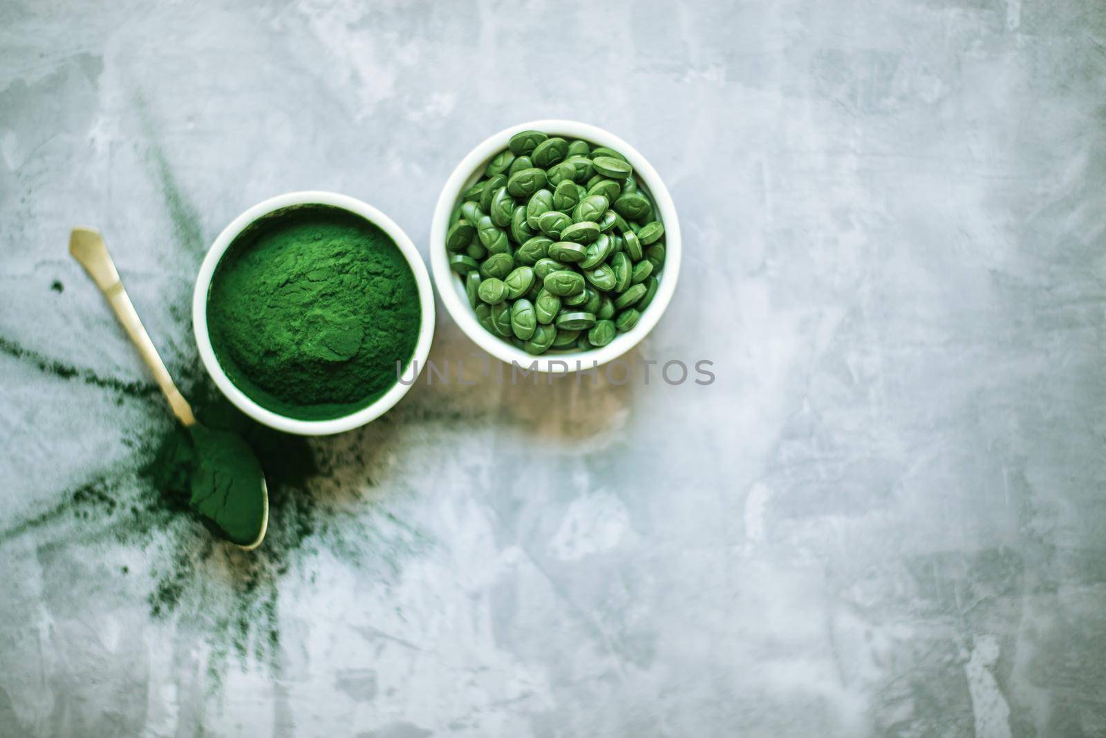 spirulina powder and tablets in white plates on concrete background. top view