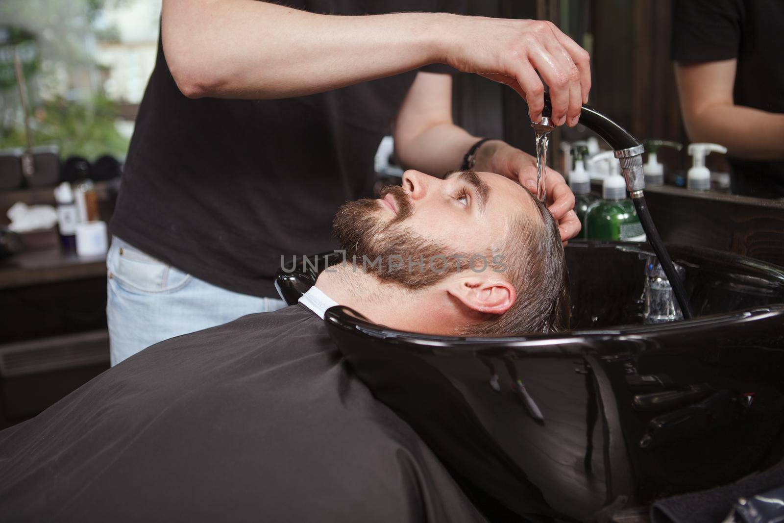 Unrecognizable barber washing hair of male client prior to haircut