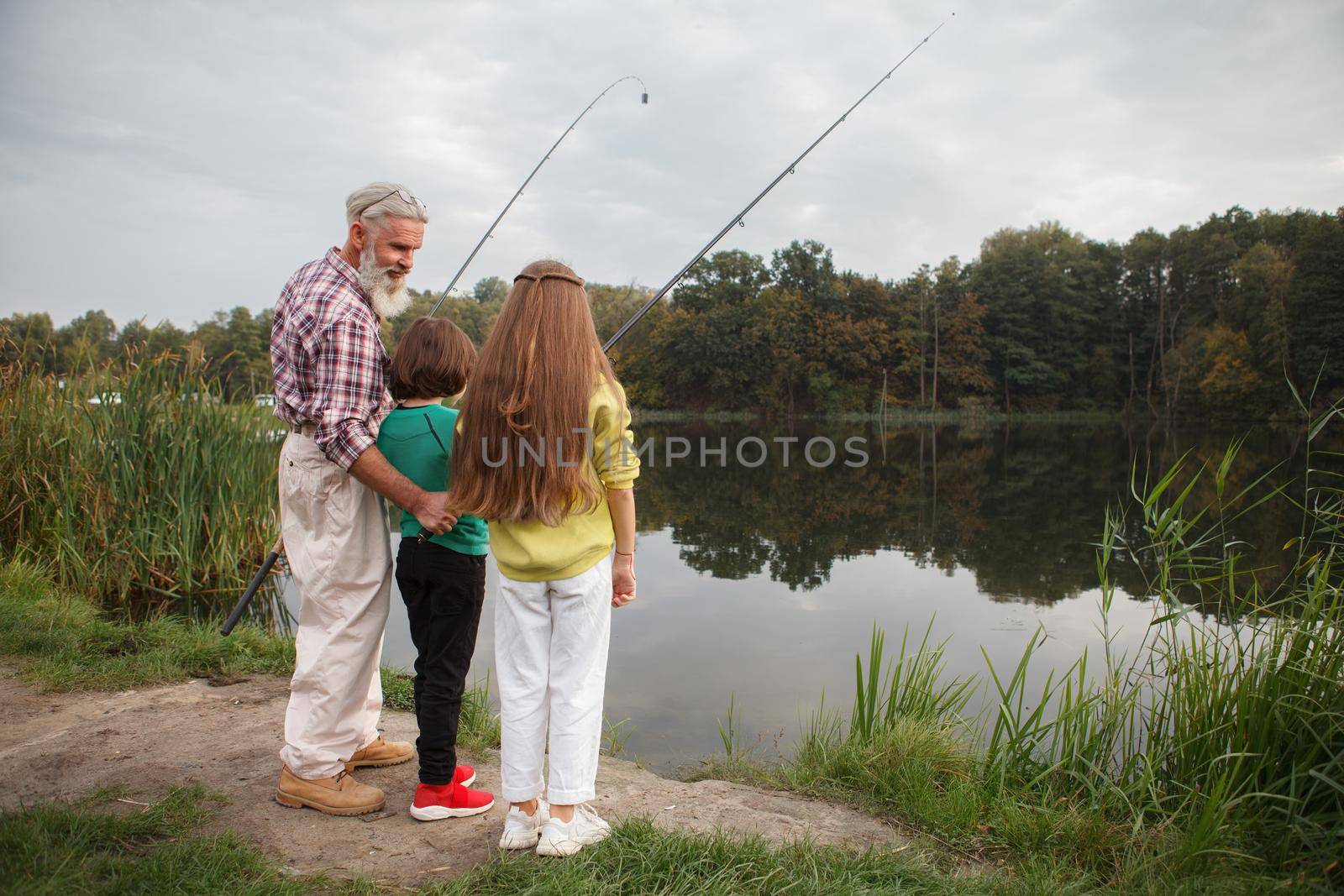 Full length rear view shot of two kids fishing on the lake with their grandfather, copy space
