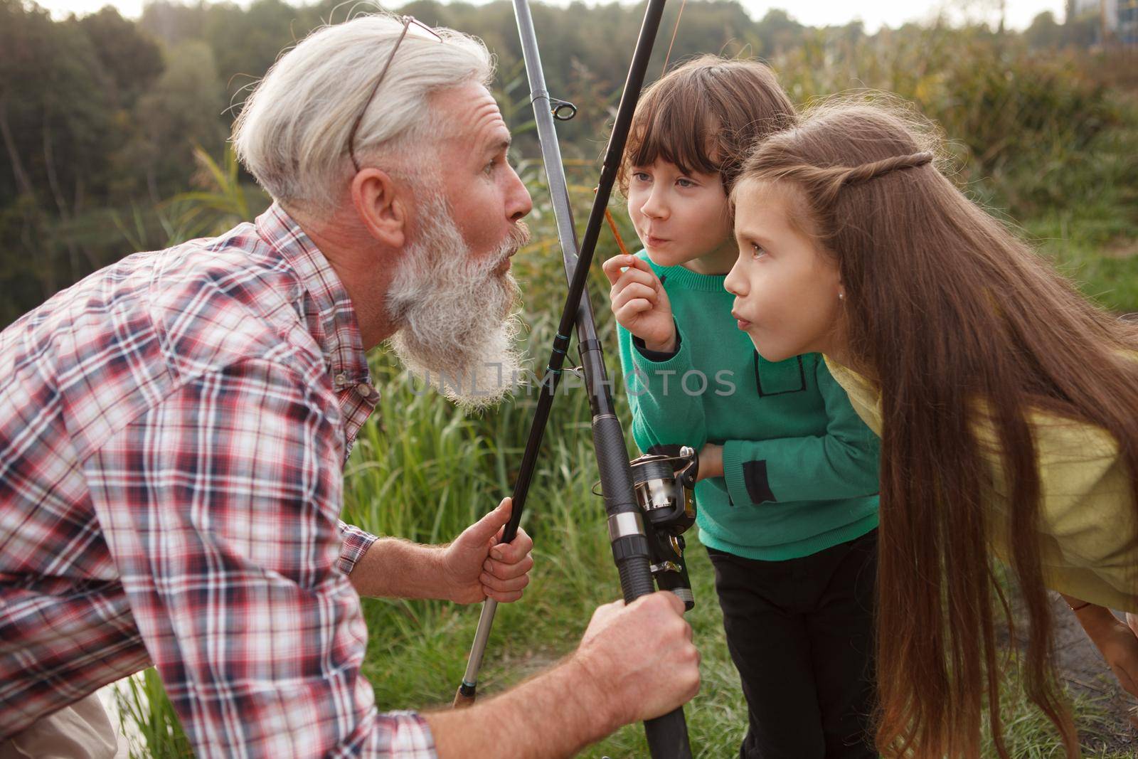 Two young kids having fun with their grandfather outdoors while fishing together