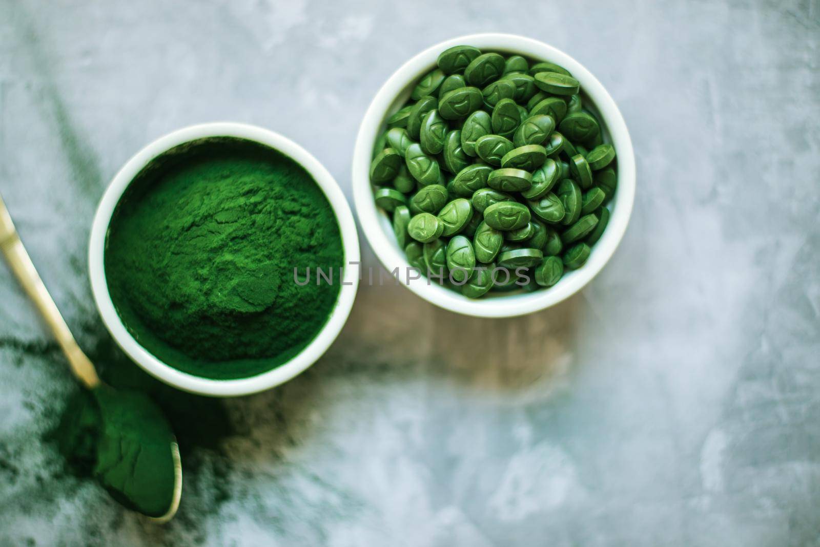 spirulina powder and tablets in white plates on concrete background by maramorosz
