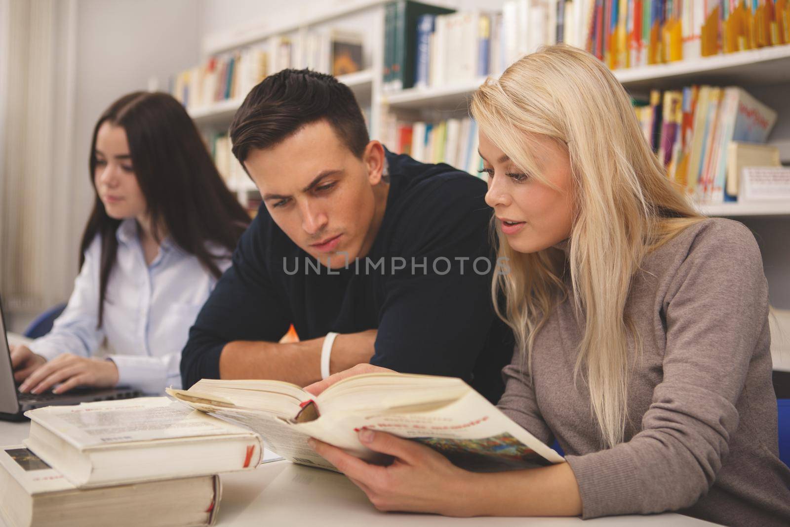 Group of college friends reading books at campus library, preparing for exams together. University students working on a project, reading and discussing ideas. Friendship, lifestyle concept