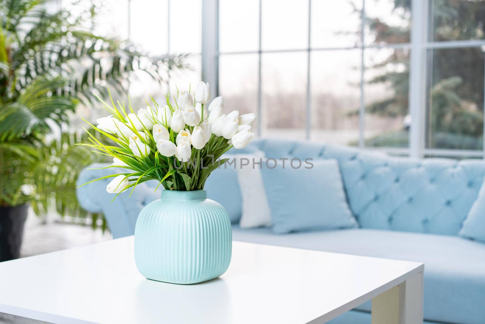 Luxury house interior. ELegant living room Modern Interior design. White Living Room Tulip flowers standing vase on coffee table With big panoramic window on background