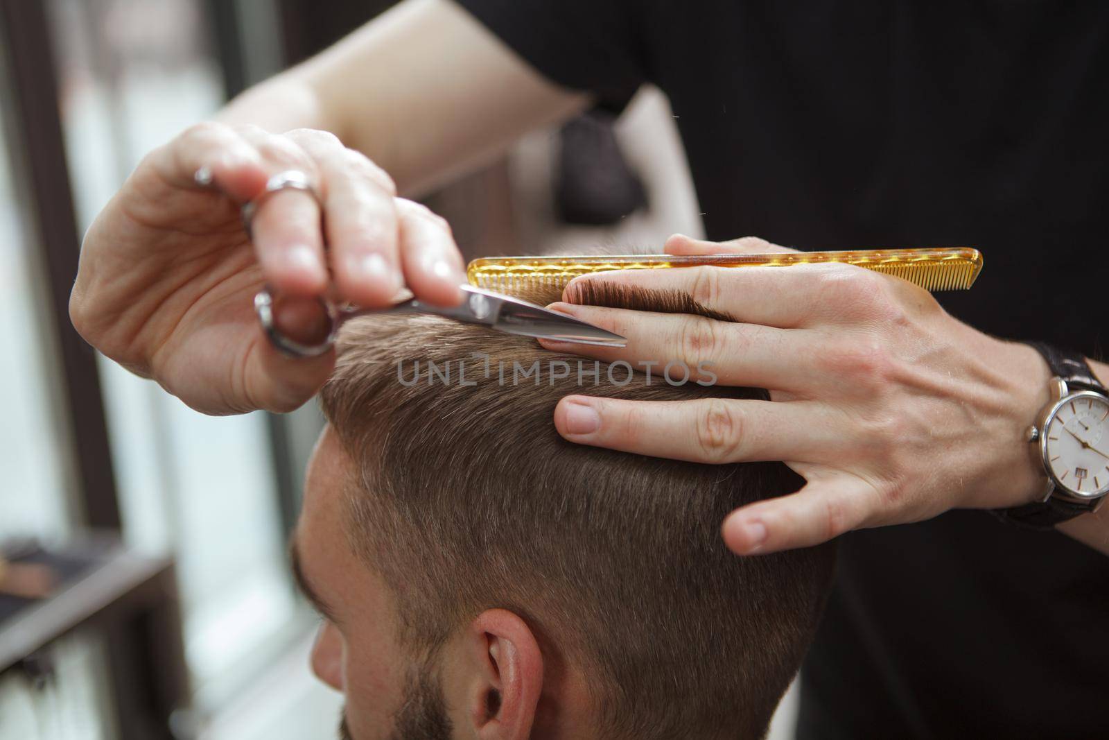 Cropped close up of a barber cutting hair of male client with scissors