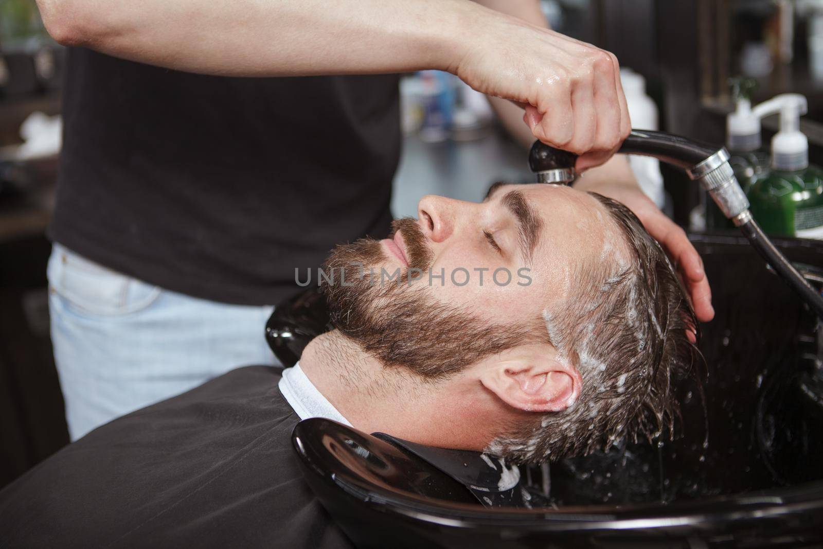 Bearded man enjoying hair wash by professional barber at the salon