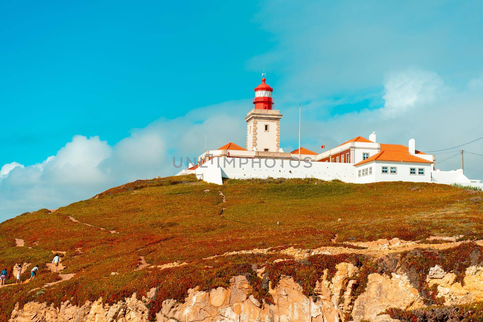 View of the Cabo da Roca Lighthouse. Sintra, Portugal. Portuguese Farol de Cabo da Roca is a cape which forms the westernmost point Eurasian land mass. Sunny summer day. Cloudy sky