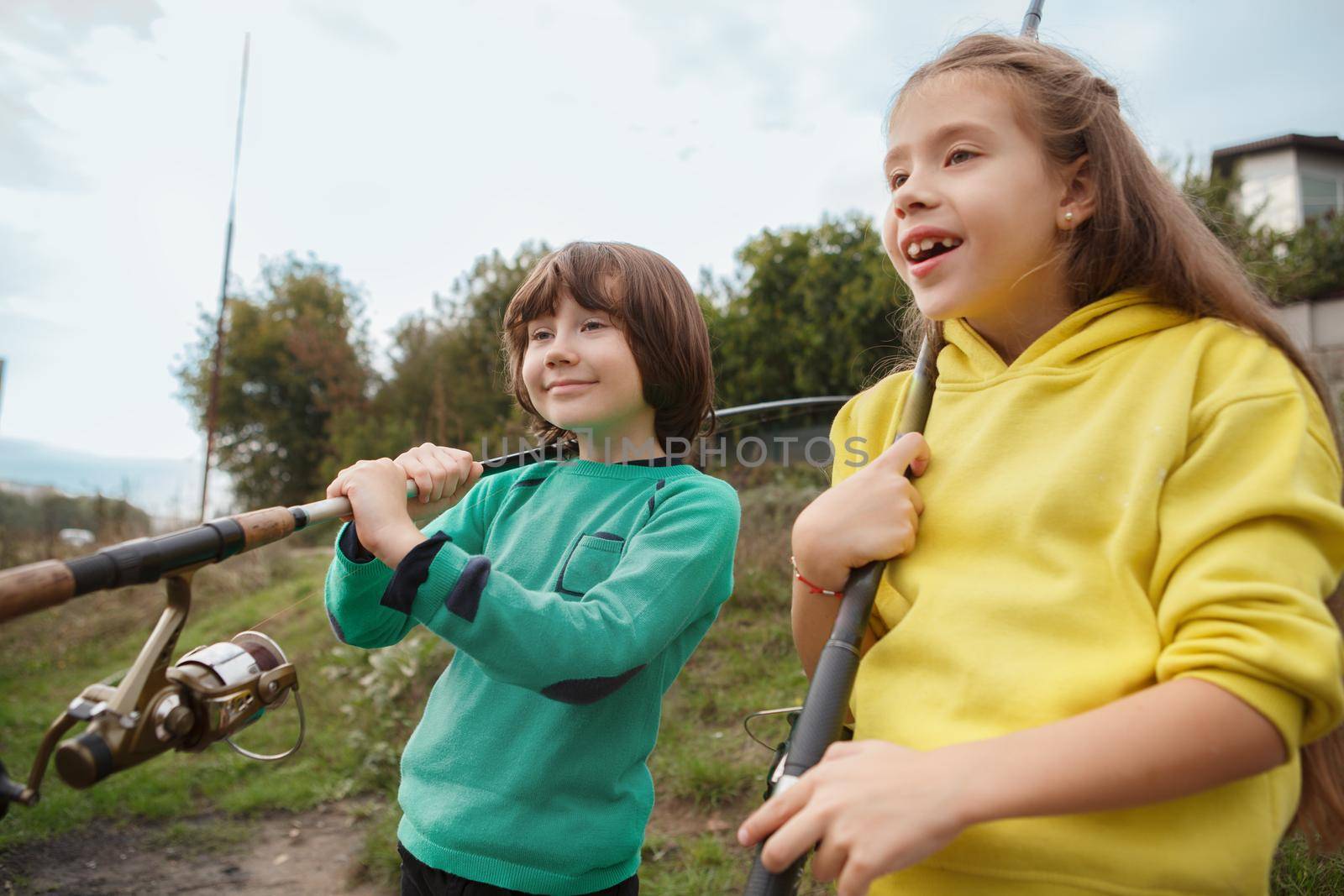 Adorable happy children holding fishing rods looking away at the lake cheerfully