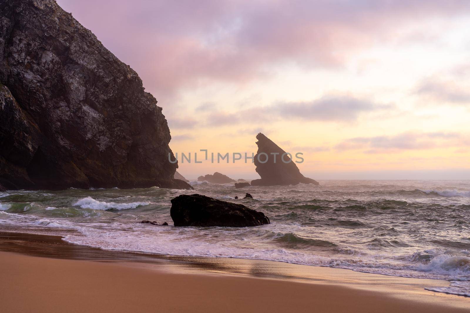 Sunset on the Ocean wild beach stormy weather. Praia da Adraga sandy beach with picturesque landscape background, Sintra Cascais Portugal Vitality of blue energy and clear ocean water