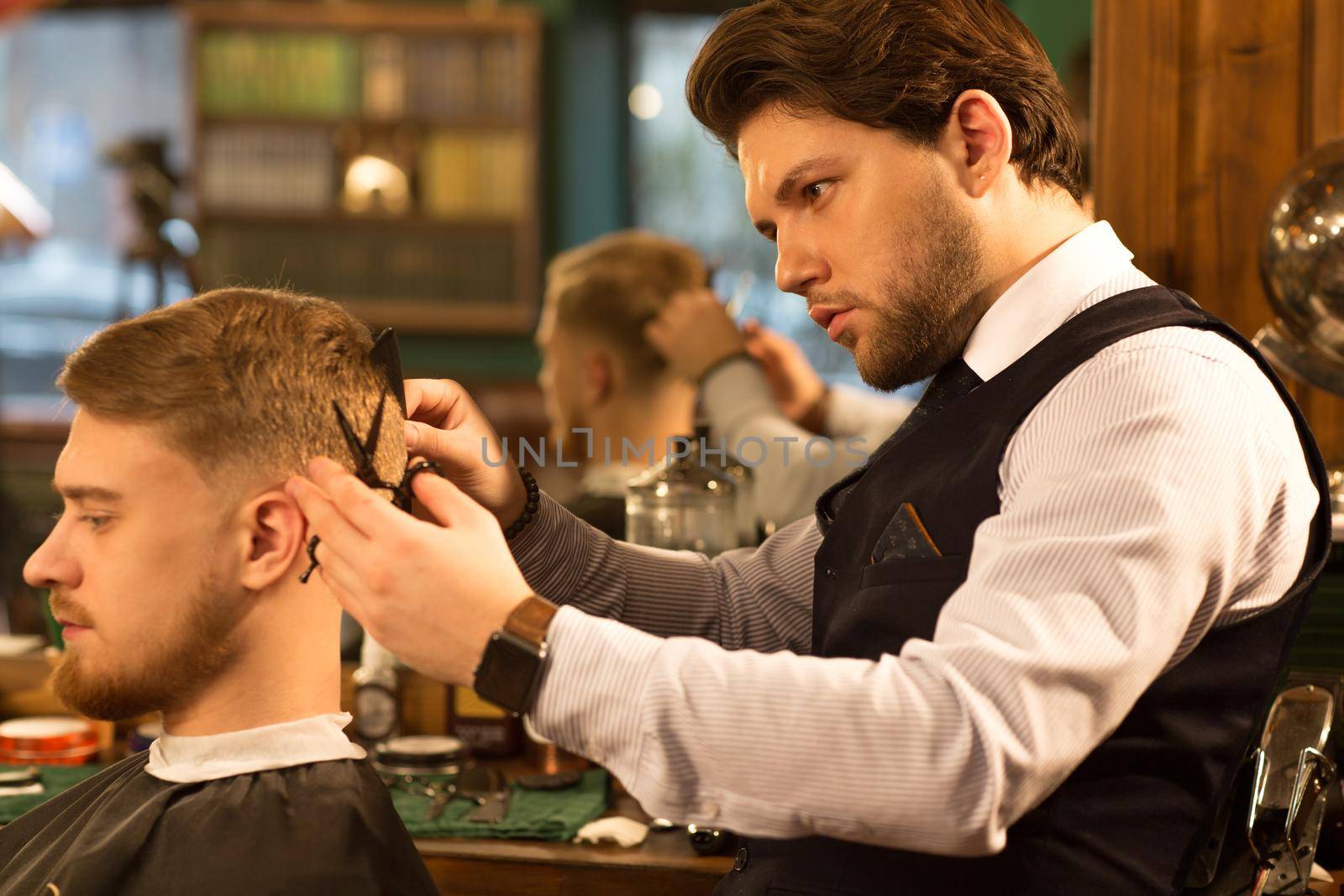 Profile shot of a handsome bearded professional barber working at his barbershop with a client cutting his hair professionalism experience concentration masculinity barbering hairdressing hairstyle.