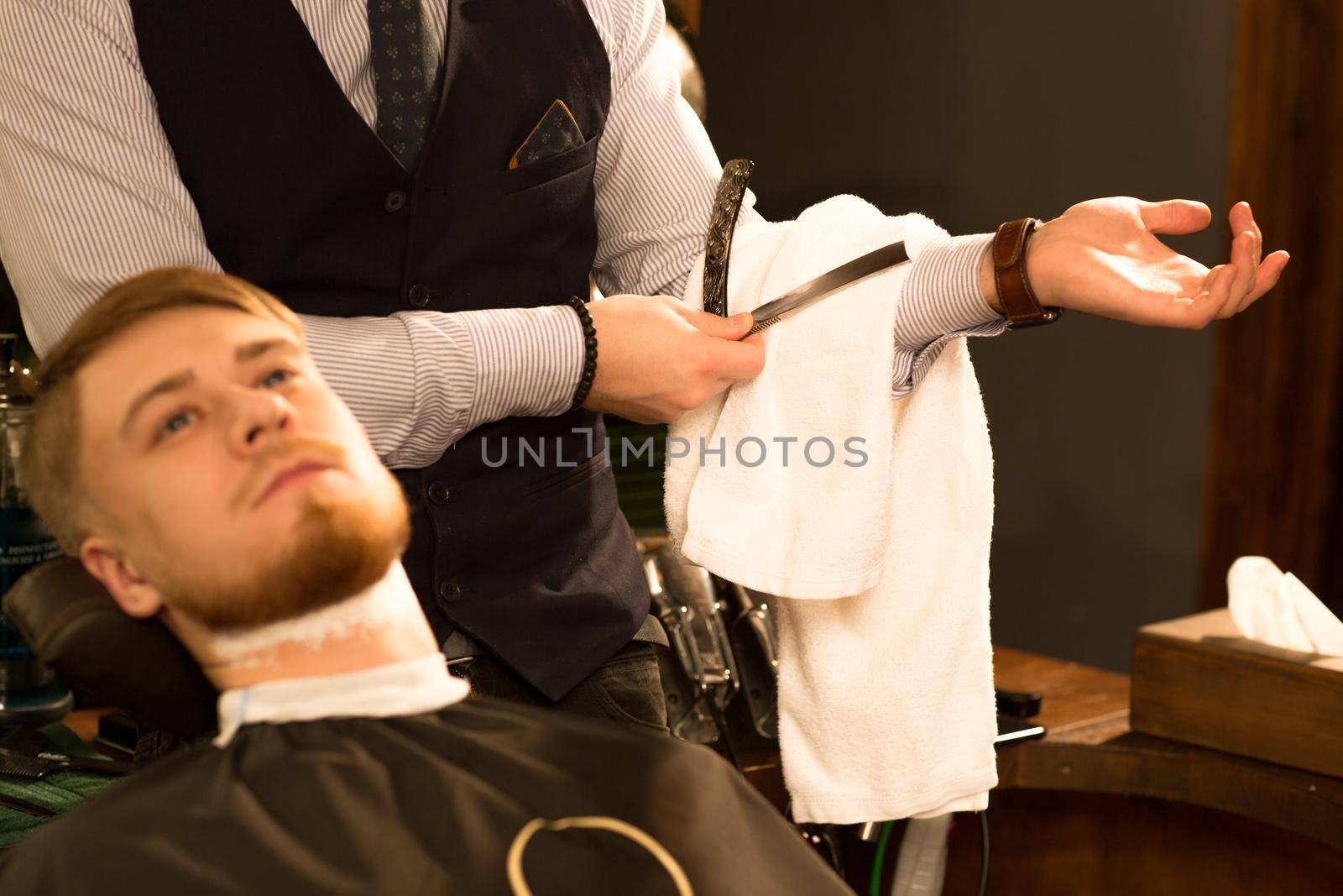 Cropped shot of a professional barber wiping shaving cream off the razor while shaving his male customer working at the barbershop occupation professionalisme experience service work job.