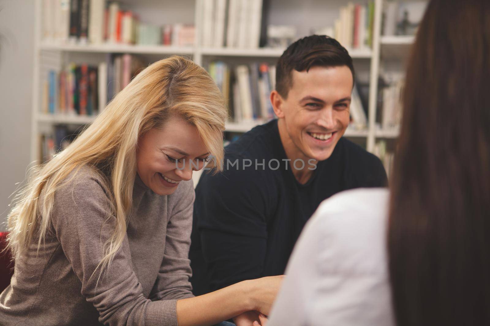 Happy college friends laughing joyfully, talking at the campus library. Cheerful male student having fun with his friends at school. Communication, lifestyle, education concept