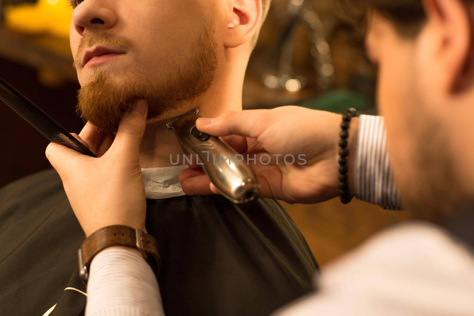 Cropped close up of a bearded man having his beard trimmed by a professional barber using trimmer clipper barbershop styling masculinity hipster service job customer client shaving barbering.