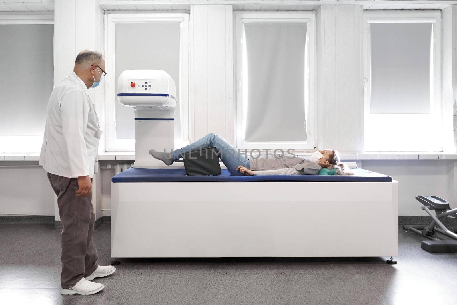 Female patient lying on a stretcher of a x-ray machine next to a female doctor with mask