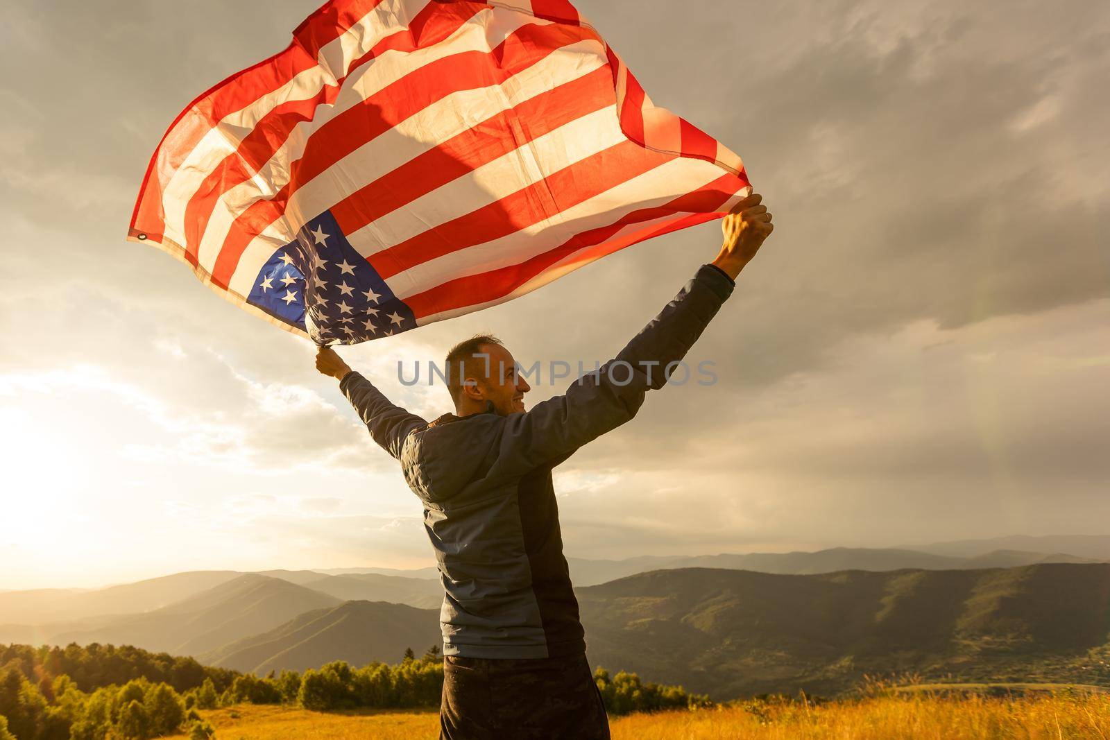 Young man proudly waving the American flag at sunset.