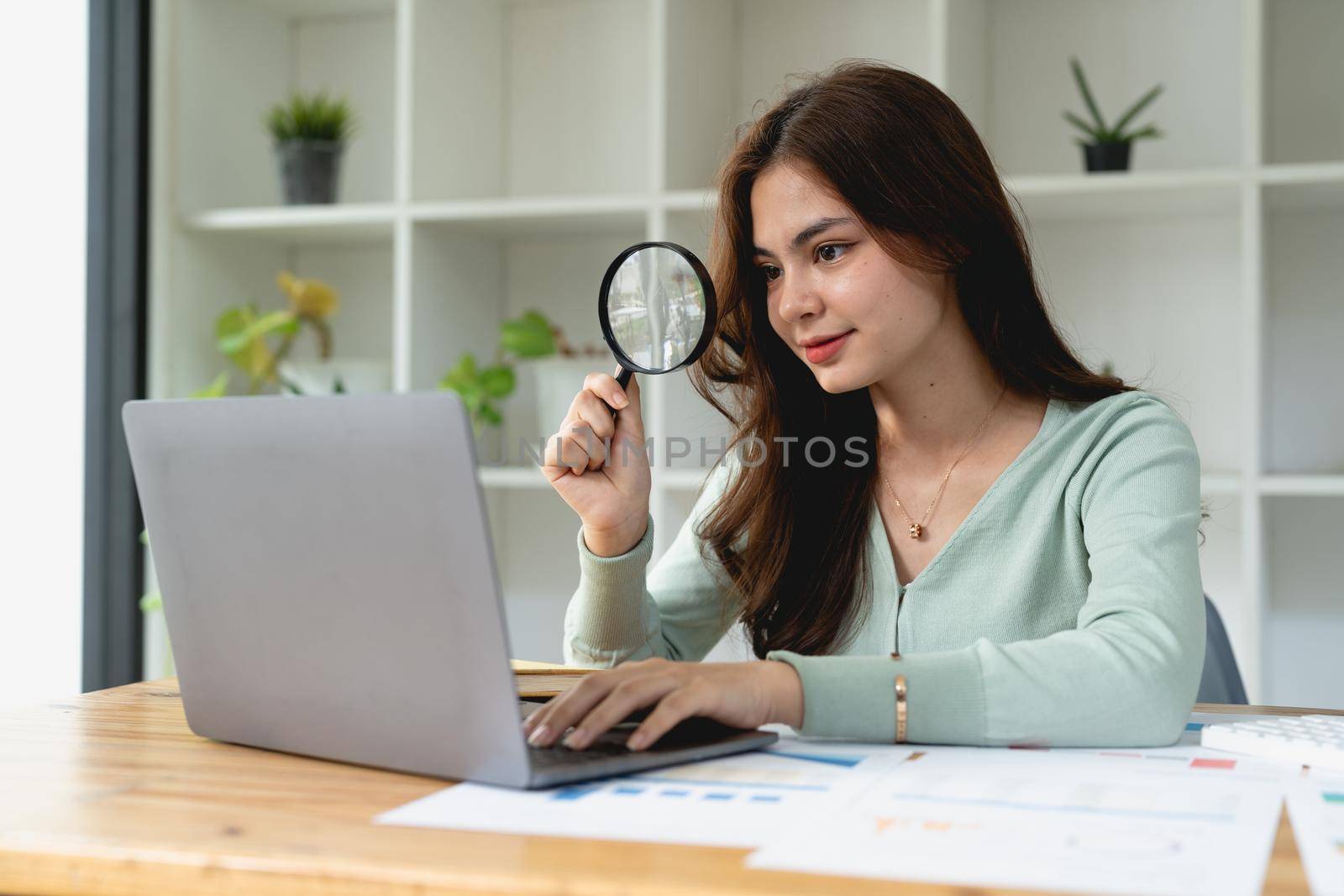 Business analyst using magnifying to review financial graphs, charts. Concept of Analyze return on investment and business analytics growth