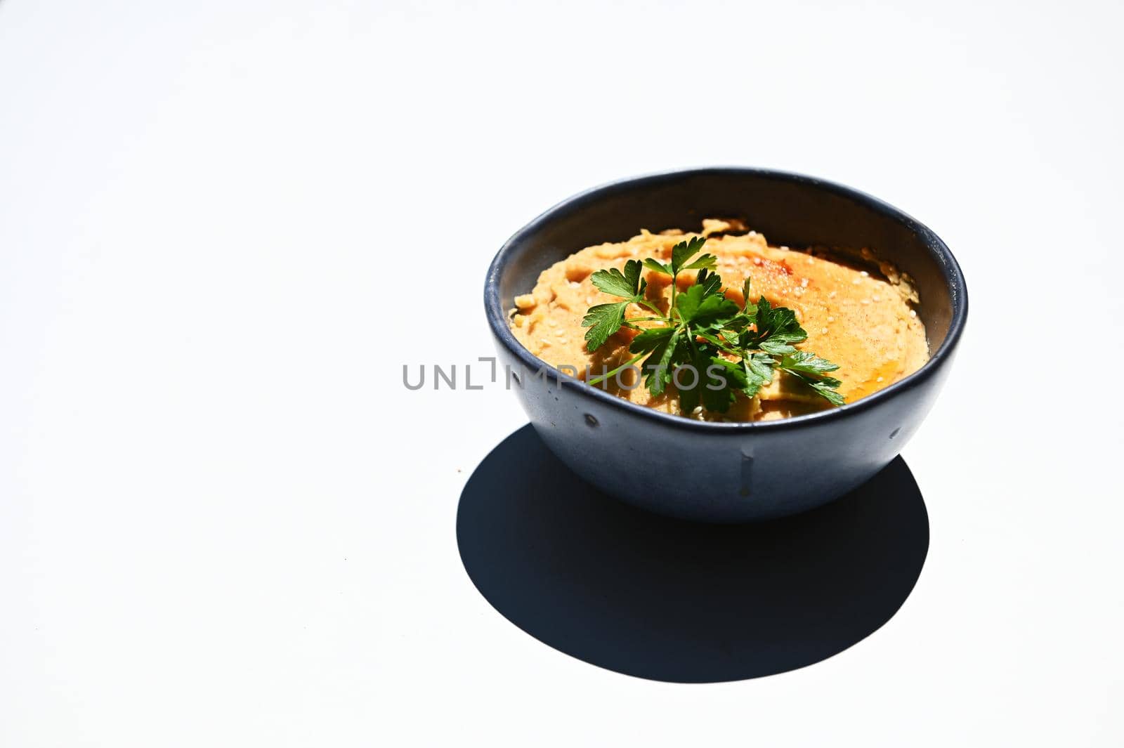 Close-up with green parsley and a bowl with topped chickpea hummus, sparkled with paprika, isolated over white background with copy space for advertising text