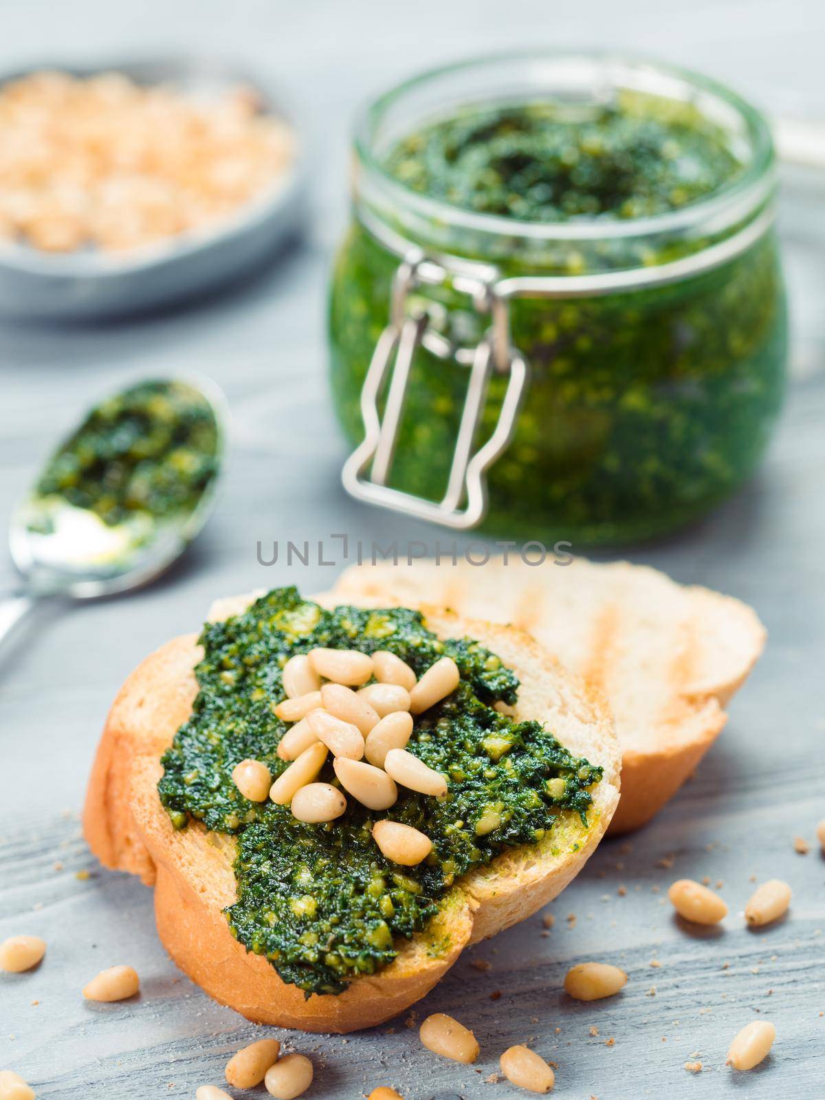 Close up view of baguette bread with fresh basil pesto sauce on gray wooden table. Copy space.