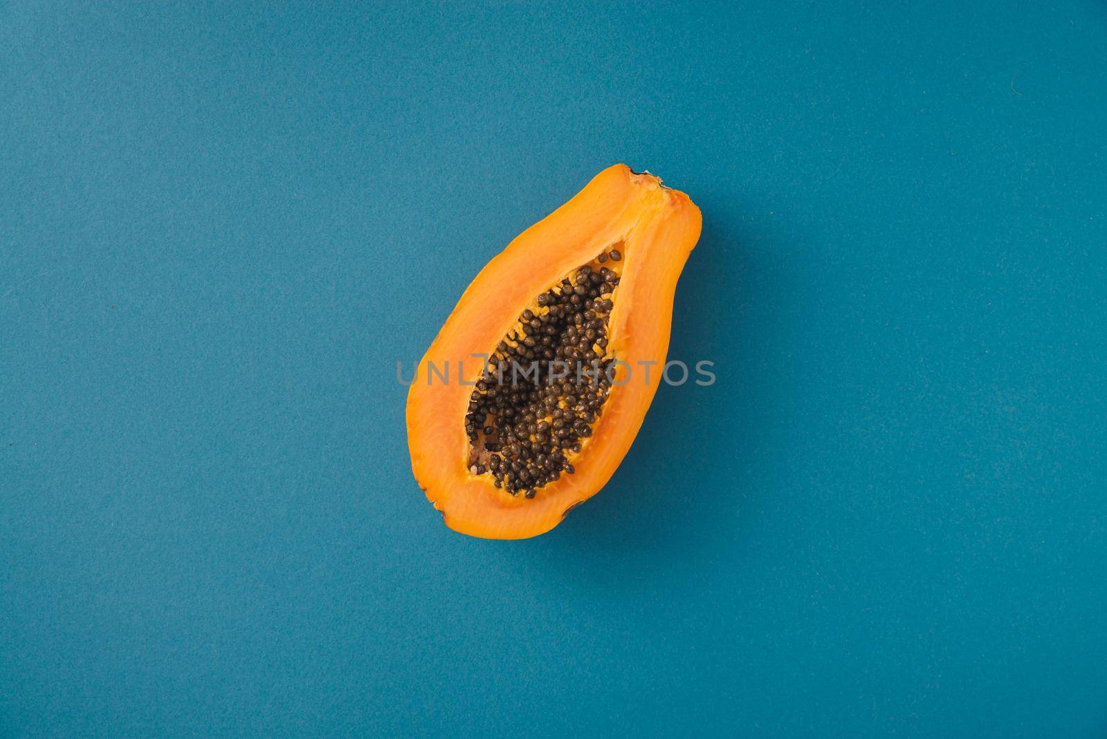 single papaya fruit cutter on half on blue background by maramorosz
