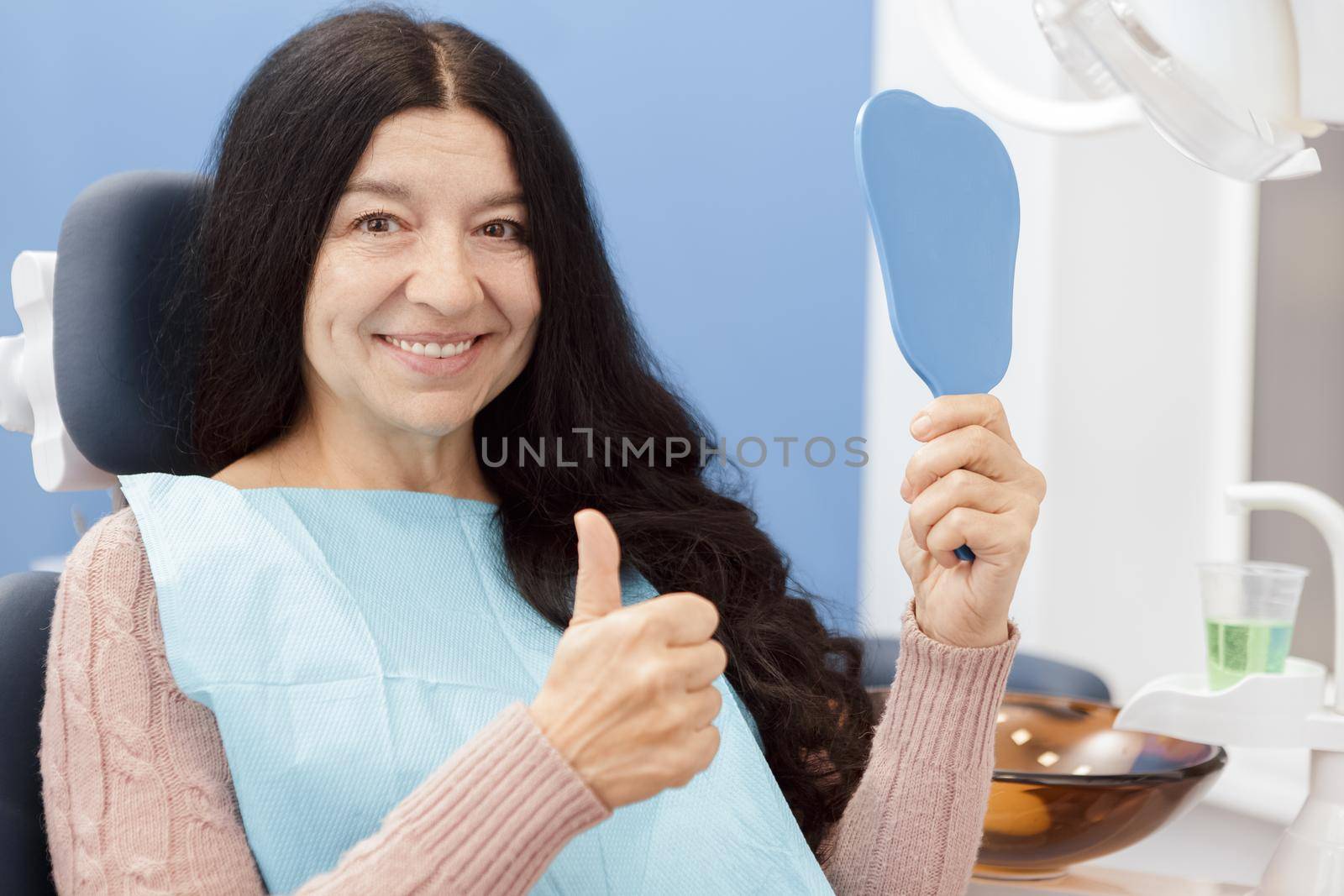 Healthy beautiful smile. Happy senior woman smiling joyfully showing thumbs up holding a mirror at the dental clinic patient client service retirement health medical industry people insurance concept