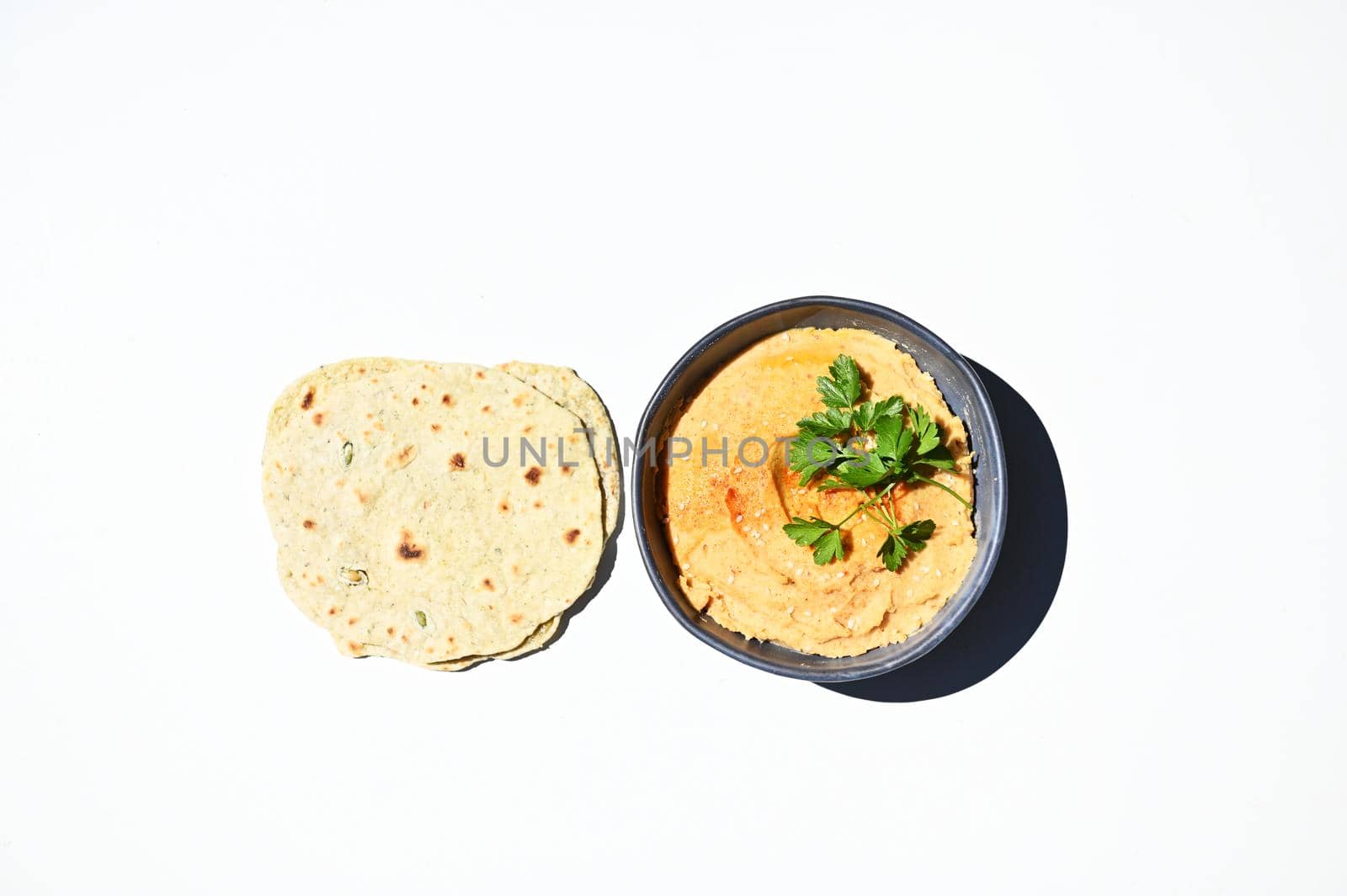 Flat lay composition with pita bread and a bowl of chickpea hummus, sprinkled with paprika, olive oil and parsley, isolated on white background with copy space for advertising text