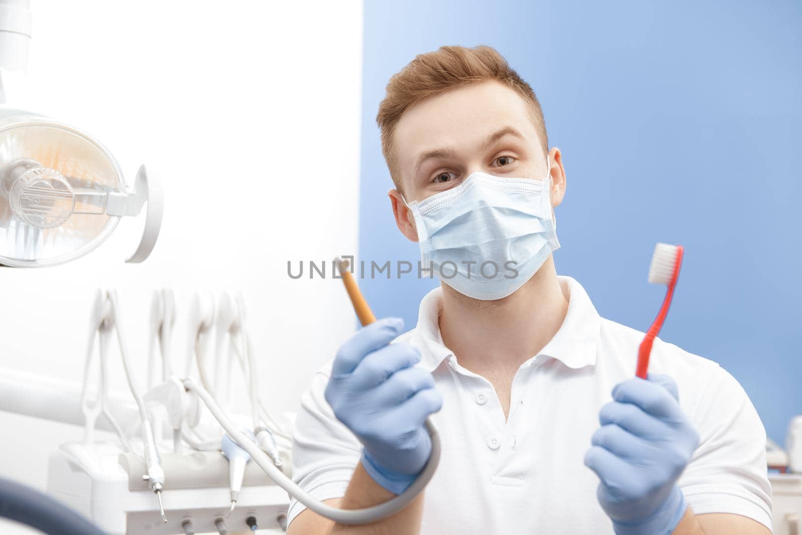Professional male dentist holding a toothbrush and a drilling machine by MAD_Production