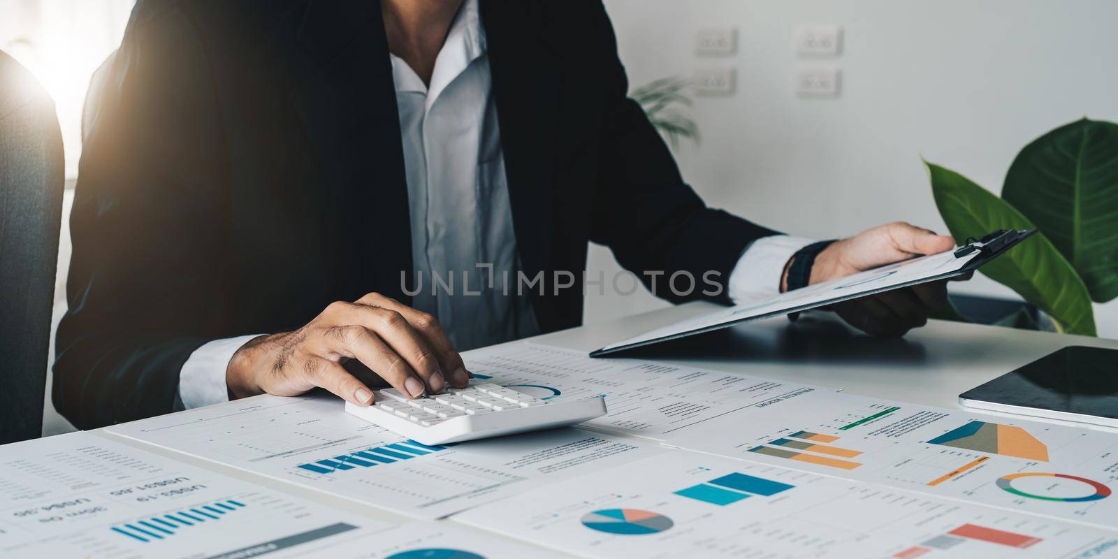Close up of businessman or accountant hand holding pen working on calculator and laptop computer to calculate business data during make note at notepad, accountancy document at office.
