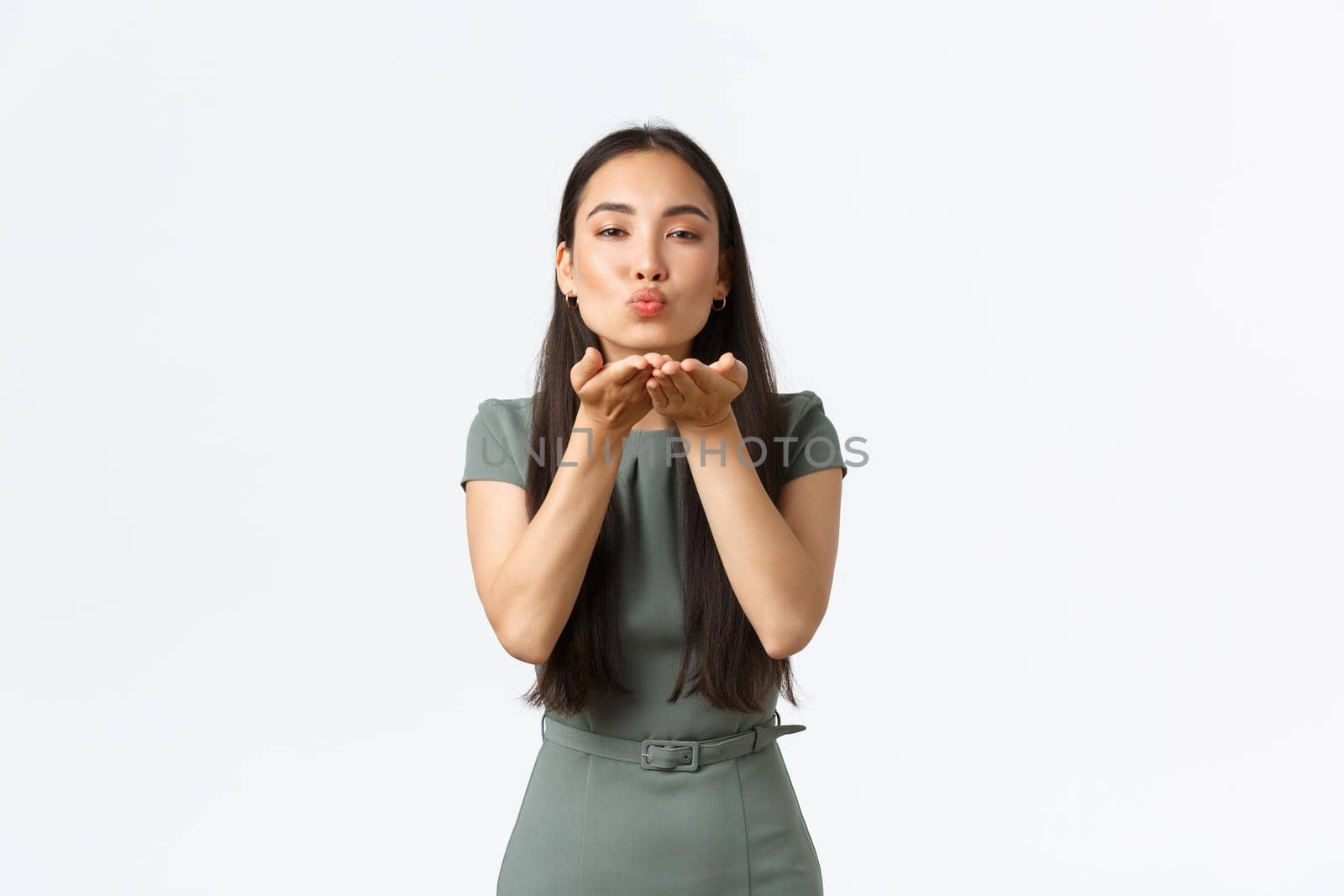 Small business owners, women entrepreneurs concept. Feminine attractive asian woman in fashionable dress, blowing mwah at camera, sending air kiss to you, standing white background.