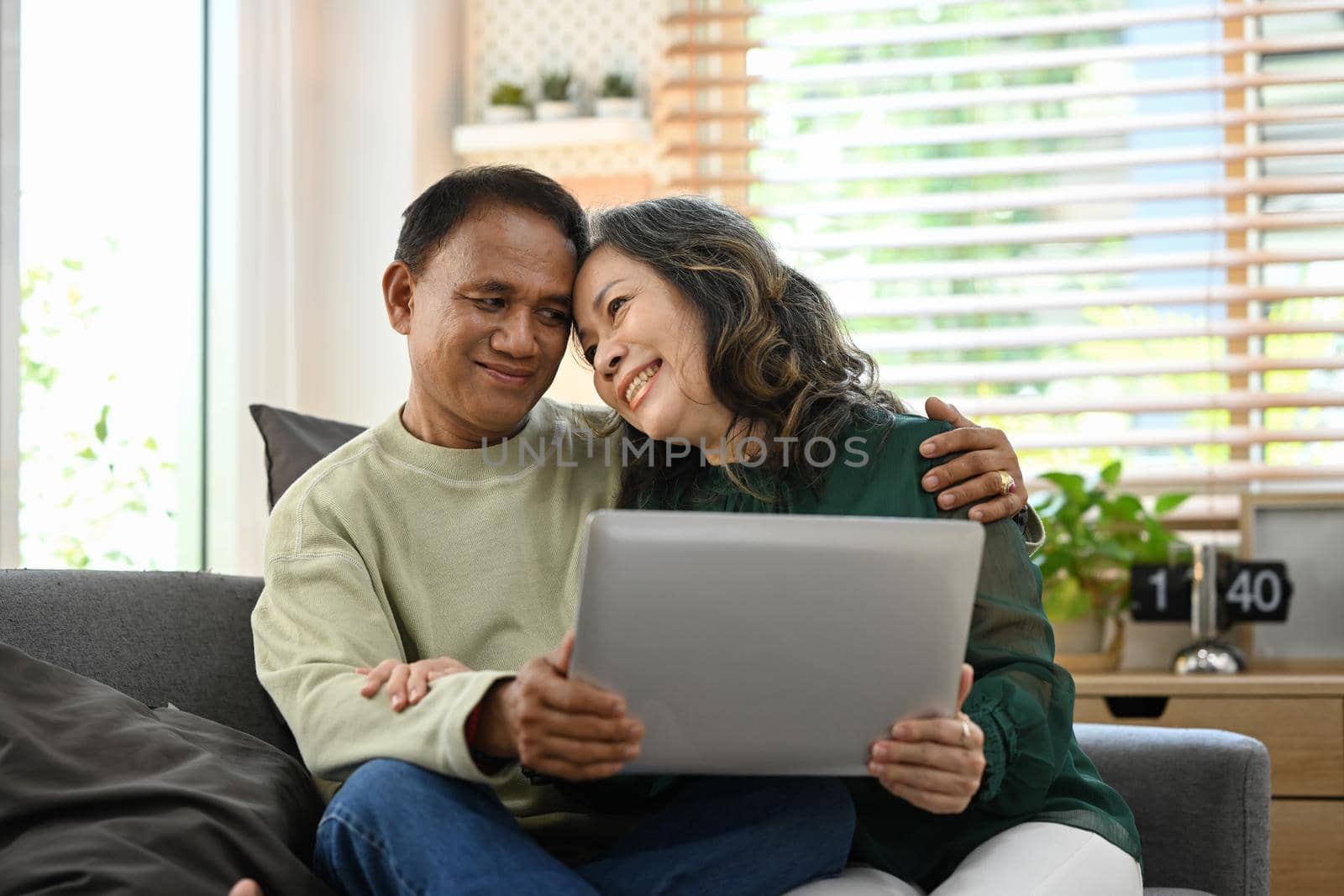 Loving senior couple relaxing on couch and using laptop, spending time together at home by prathanchorruangsak