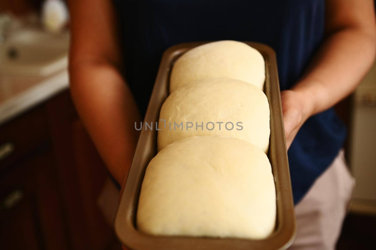 Close-up. Cropped view of the hands of a housewife holding a baking container with suitable yeast dough for bread. Culinary. Bakery. Cooking a healthy homemade whole grain bread