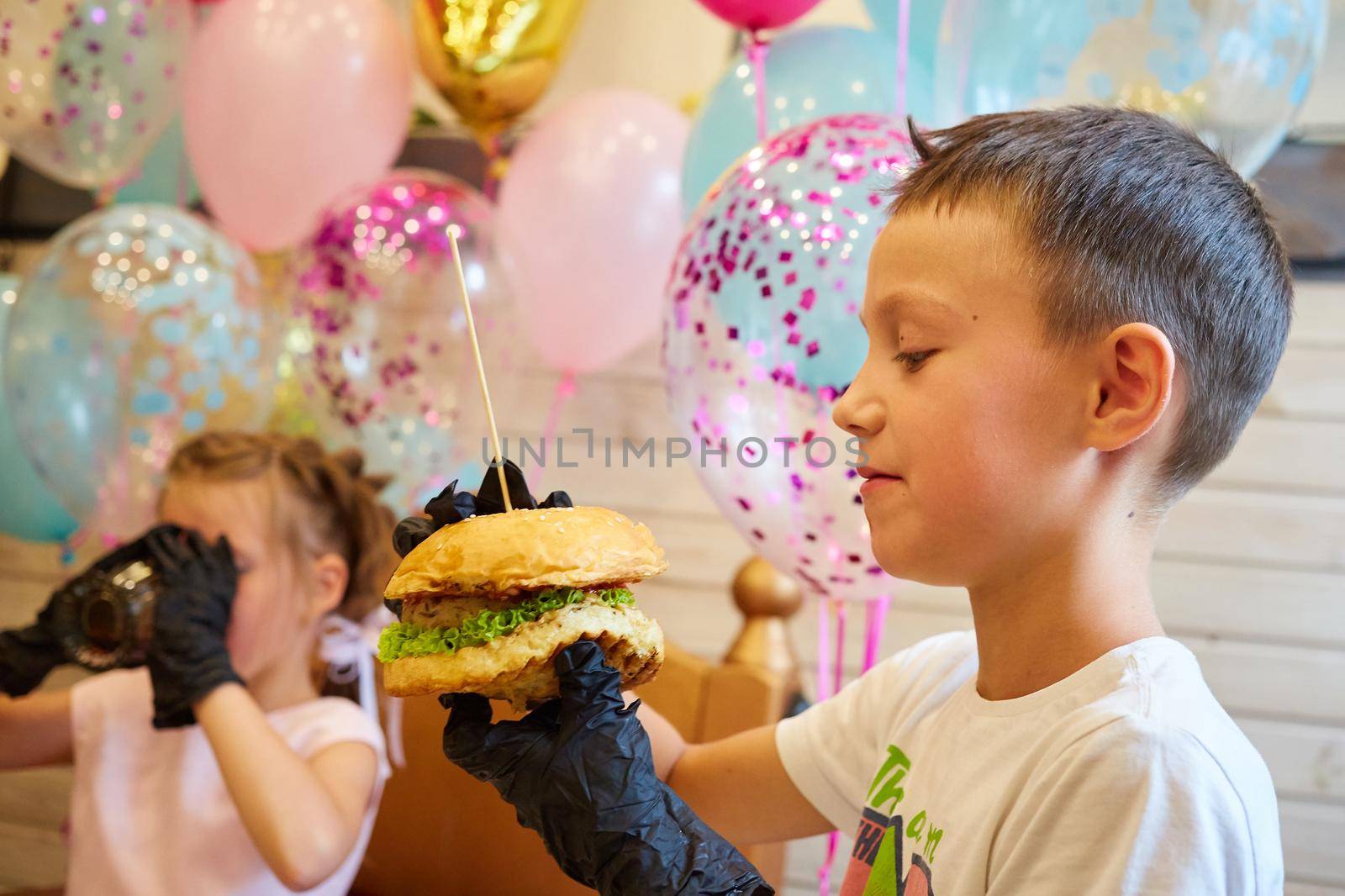The handsome little boy eating burger in black rubber gloves