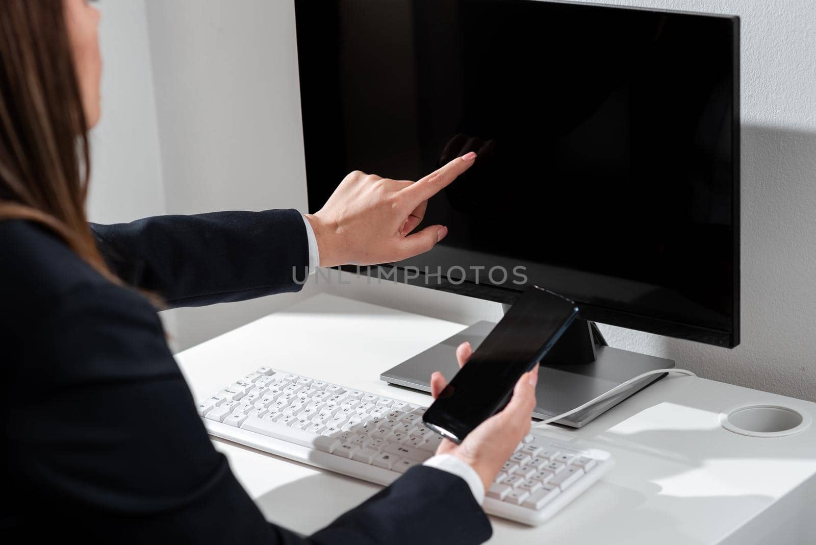 Businesswoman Holding Mobile Phone And Pointing On Computer Screen.