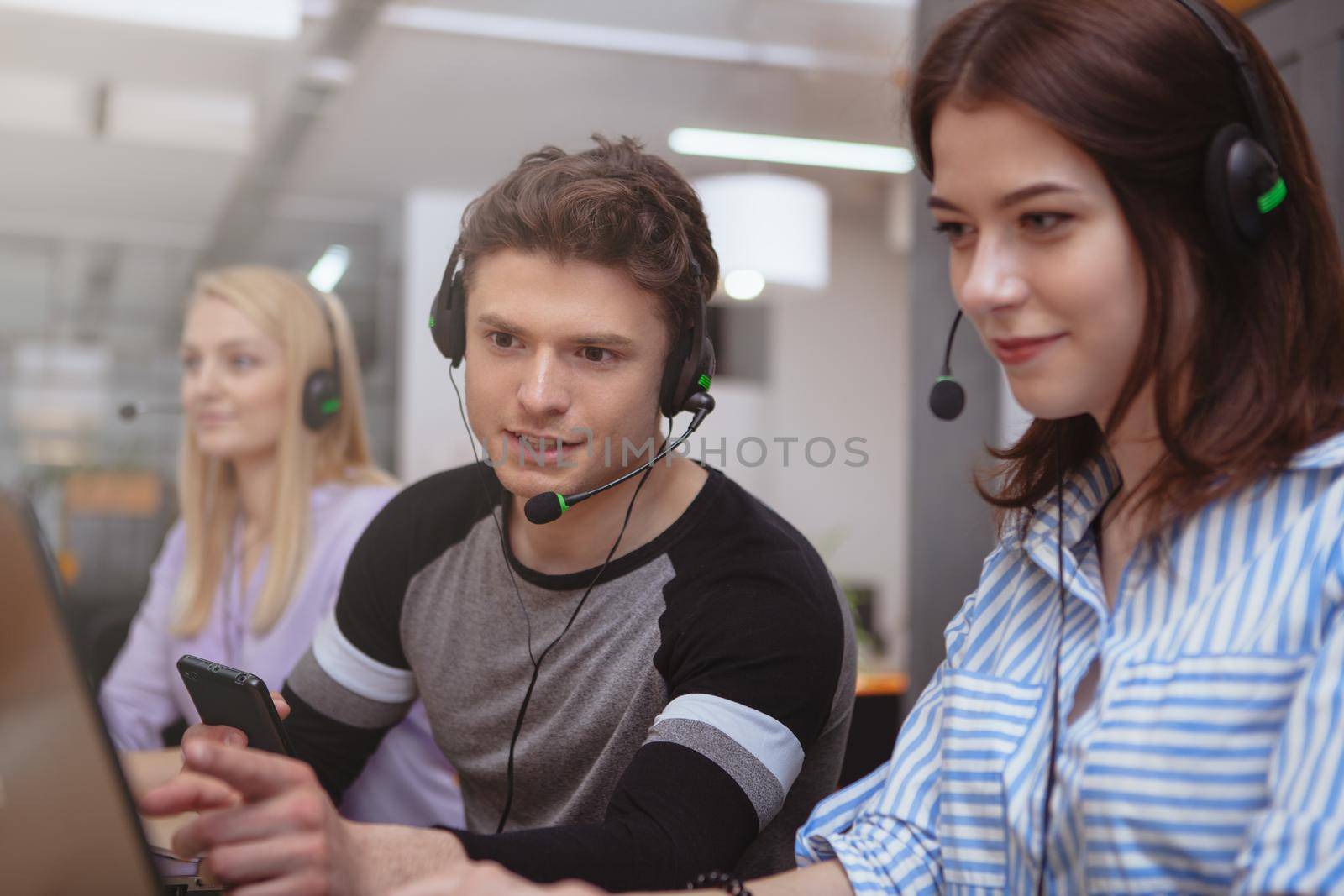 Group of young people working at customer services call center. Handsome male call center operator talking to his colleague while working. Client services operators with headsets working on computers