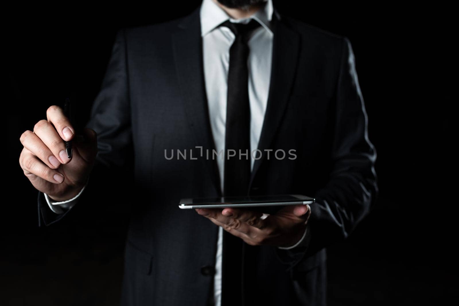 Businessman Holding Tablet In One Hand With Other Pointing Important Message With Pen. Executive In Suit Having Cellphone In One Palm And Crutial Announcement In Another. by nialowwa