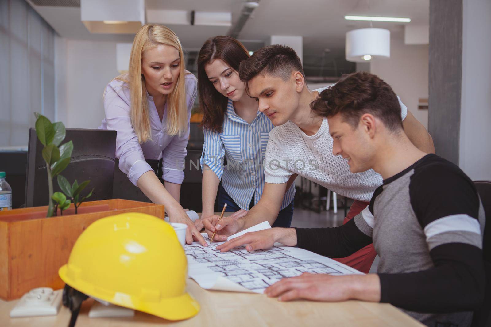 Group of young architects examining architectural blueprints together, copy space. Professional engineers working on a building plan at the office. Teamwork, design concept