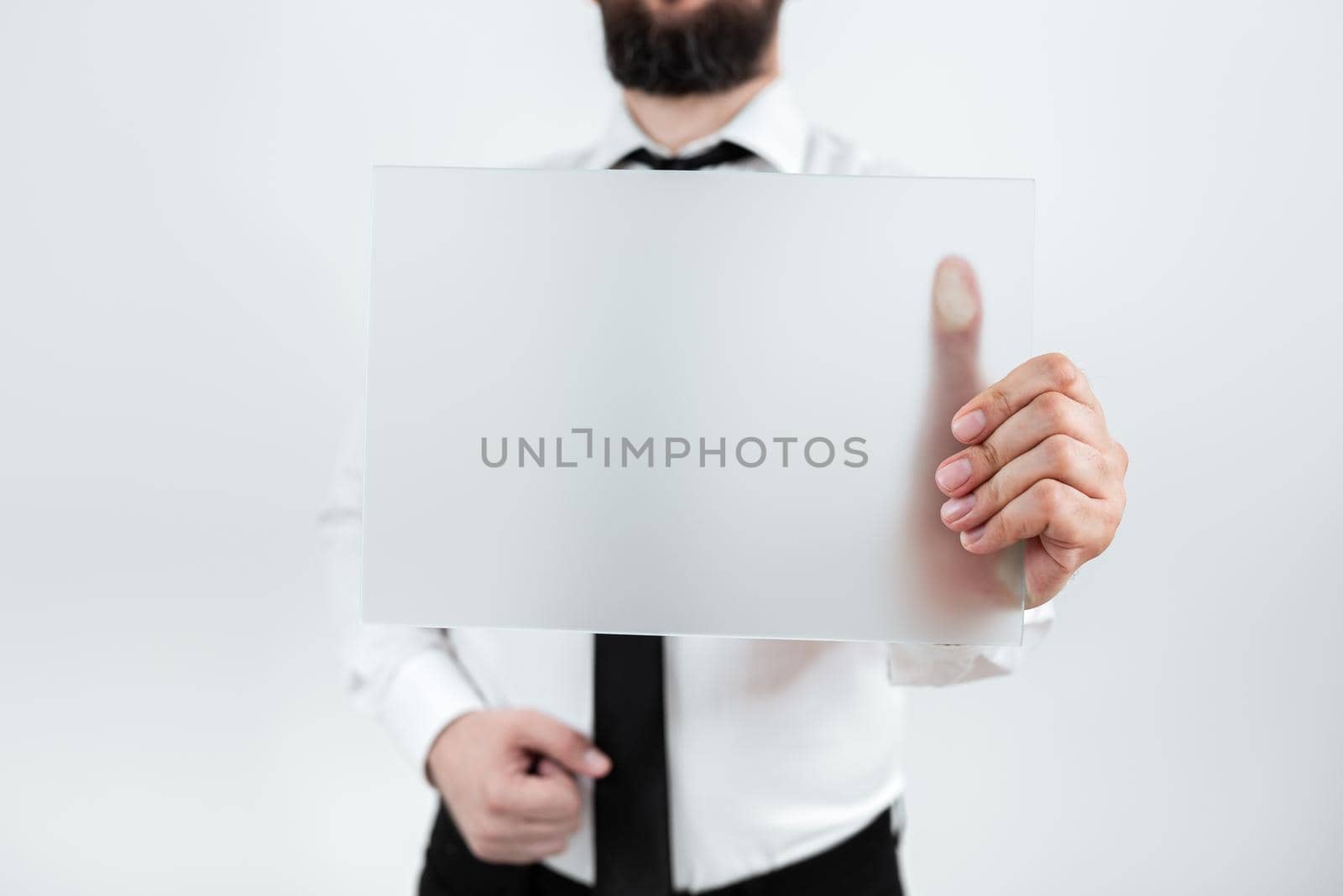 Male Professional Holding Blank Placard And Showing Important Data. Businessman With Paper In Hands Presenting Marketing Strategies For Development Of Business. by nialowwa