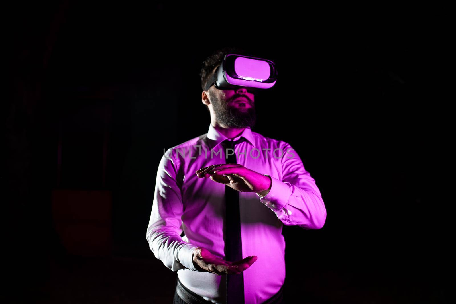 Businessman Using Virtual Reality Goggles Gesturing While Taking Professional Training. Light Falling On Man Experiencing Simulator And Presenting Modern Technology. by nialowwa