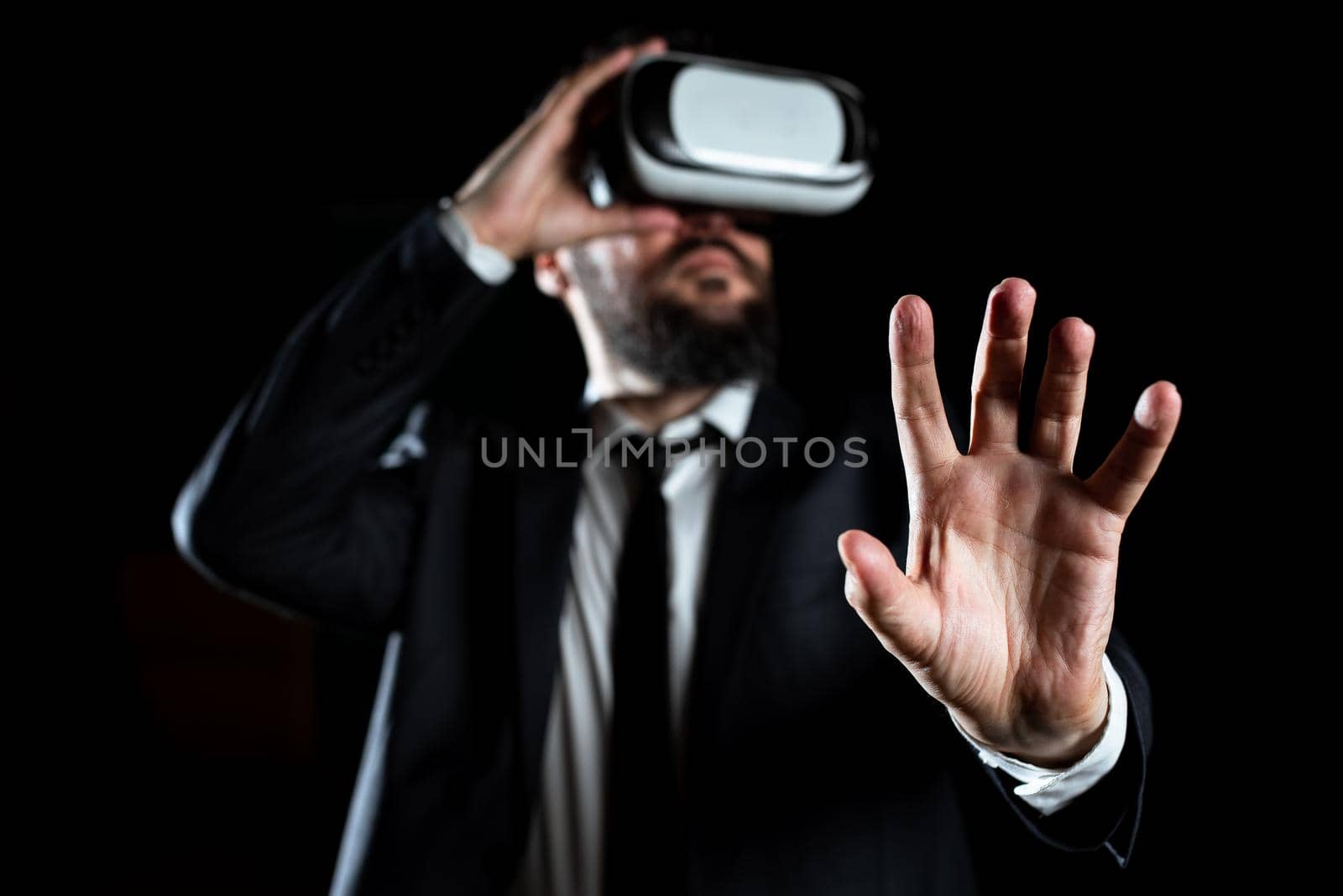 Male Professional Wearing Virtual Reality Goggles Gesturing And Introducing Modern Technology Of Learning. Businessman Wearing Suit Taking Training Through Simulator. by nialowwa