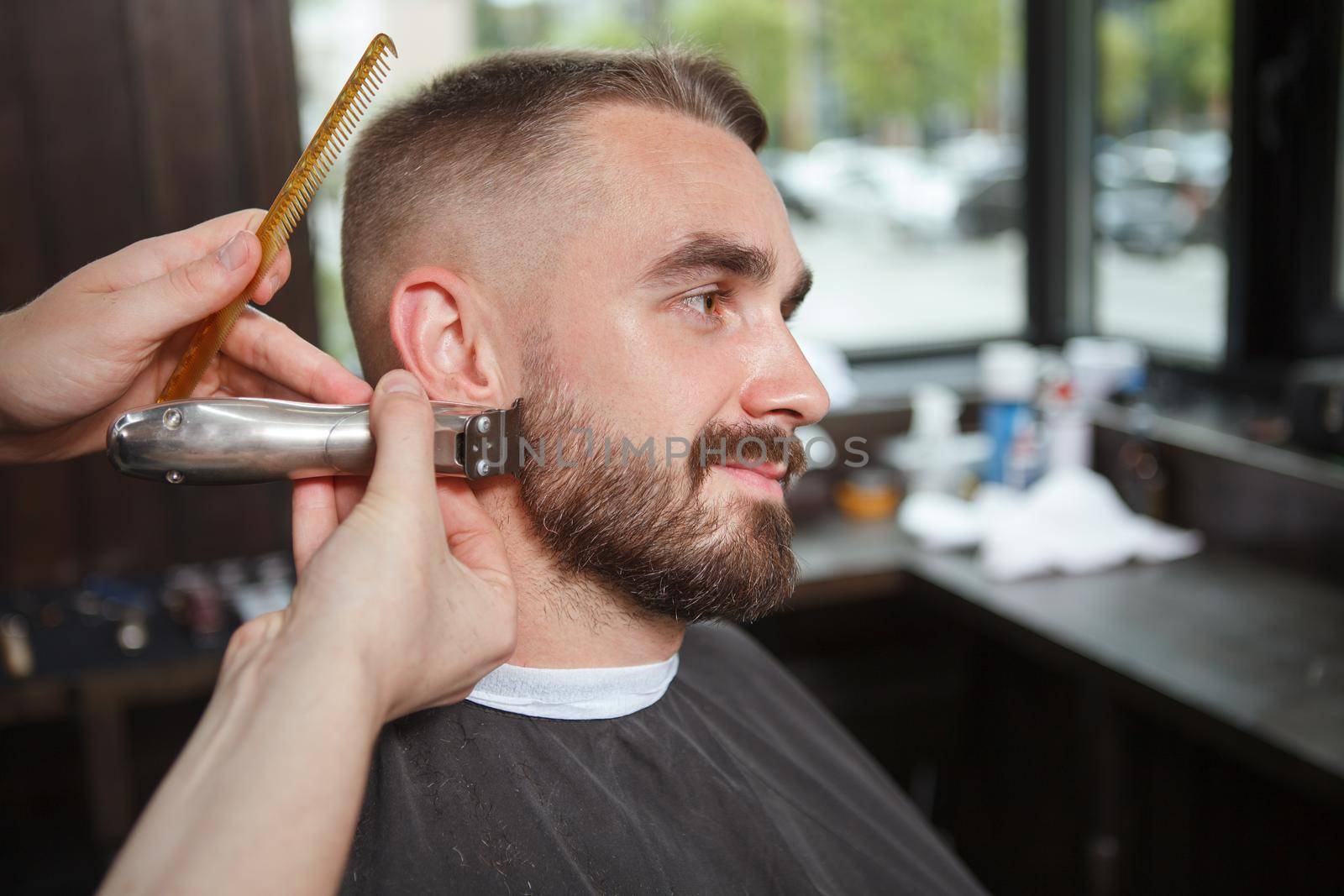 Close up of a barber shaping beard of male customer