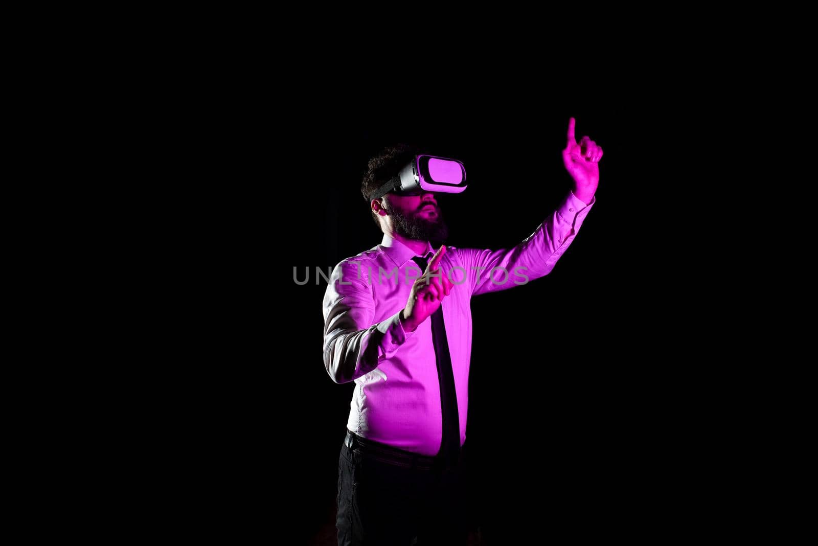 Businessman Using Virtual Reality Goggles Gesturing While Taking Professional Training. Light Falling On Man Experiencing Simulator And Presenting Modern Technology. by nialowwa