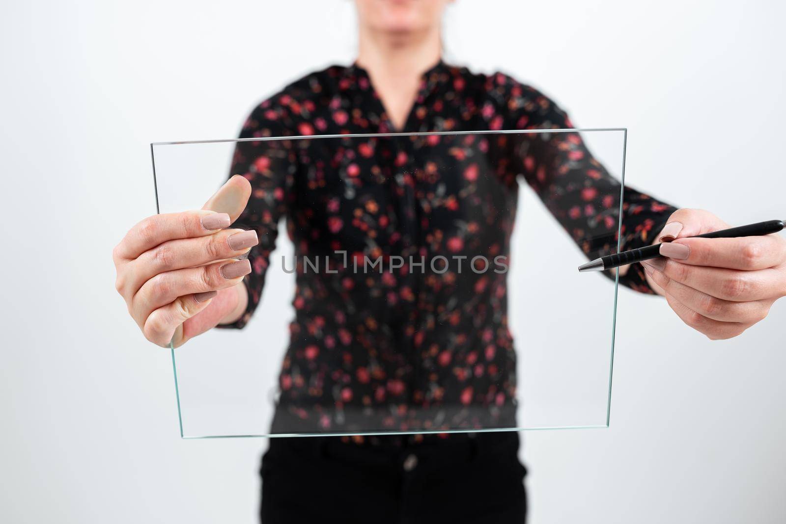 Businesswoman Holding Pen And Transparent Glass While Presenting Important Information. Woman Wearing Floral T-Shirt Showing Rectangular Banner For Brand Promotion. by nialowwa