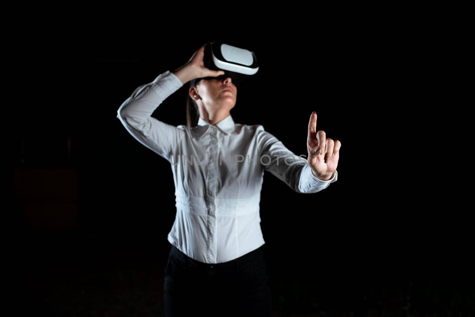 Female Professional Wearing Virtual Reality Headset Gesturing And Enjoying Simulator. Elegant Businesswoman Presenting Modern Technology And Using Futuristic Gadget. by nialowwa