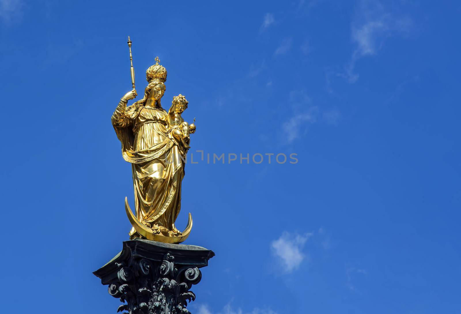 The statue of the Mariensäule on Marienplatz in Munich. The Mariensäule is a golden colored statue depicting the Madonna and Child Jesus standing on a crescent moon by rarrarorro
