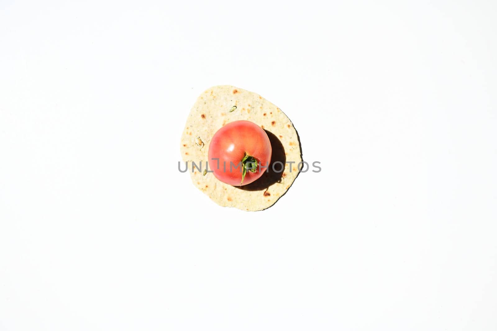 Flat lay of a ripe juicy tomato on a freshly baked homemade chapati, pita bread, flatbread, isolated over white background with copy space for advertising text. Top view, still life, food background