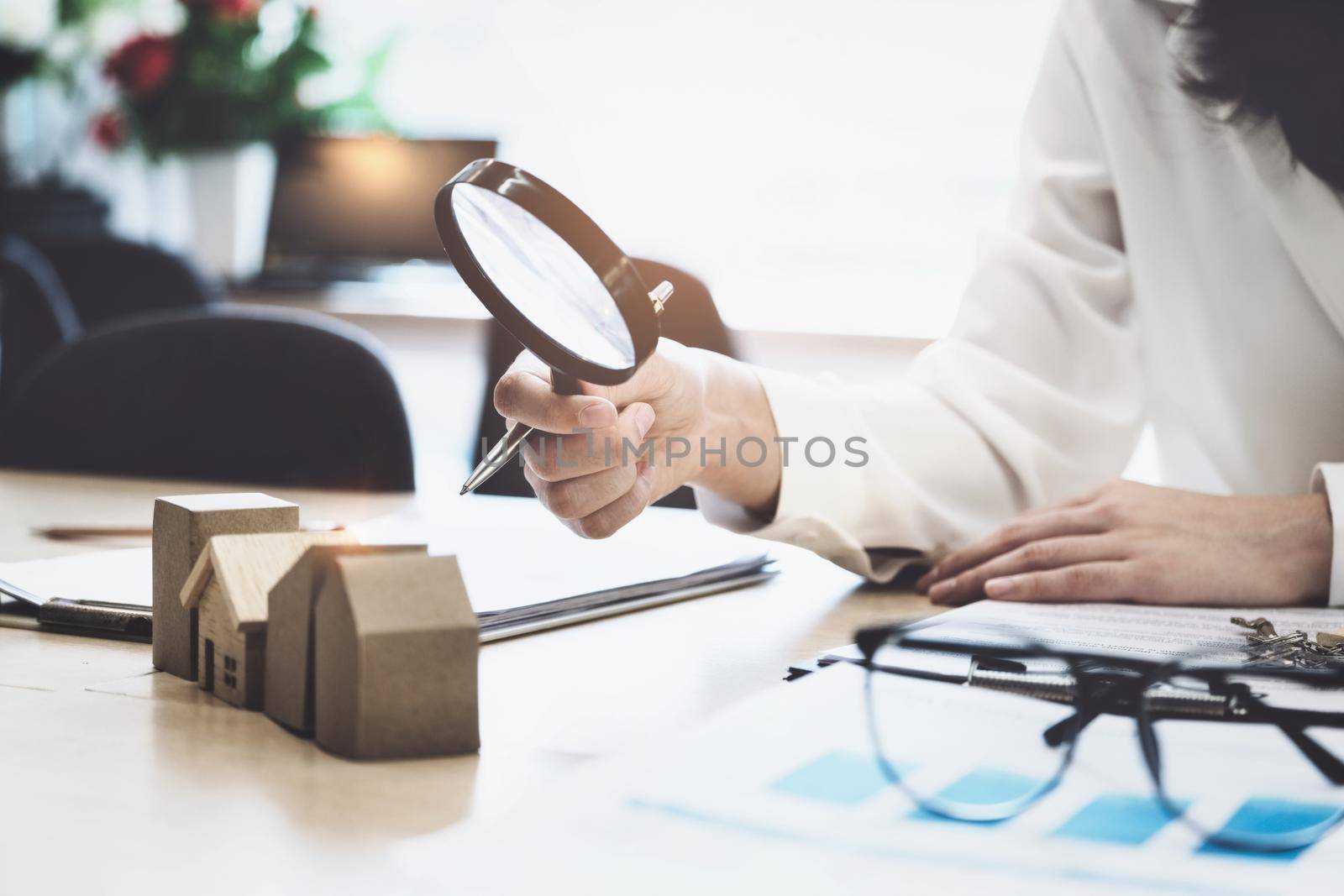 Inspector Concept, a customer is holding a magnifying glass to look at each house model to check the price of a home loan for each model